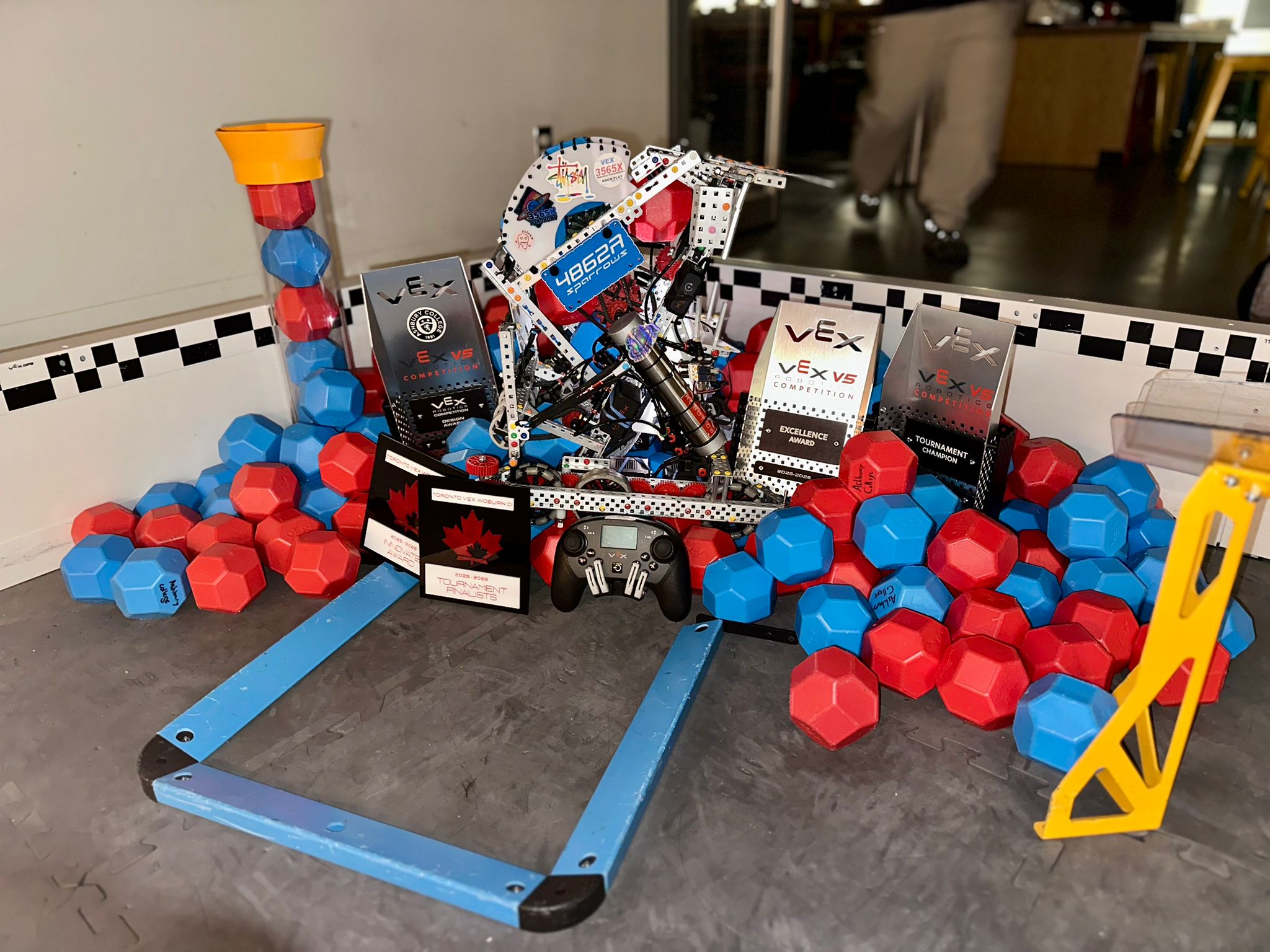 Robot surrounded by VEX V5 tournament trophies